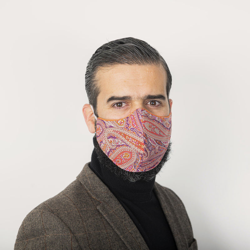 Male model wearing a sleek-fitting pink Liberty London paisley print face mask securely over his beard. The mask has orange Tana Lawn piping.