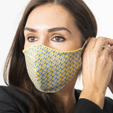 Female model adjusting a blue and mustard Liberty London print face mask. The face mask has yellow piping.